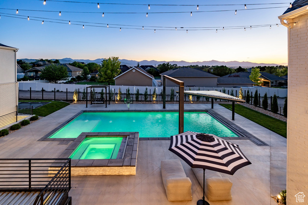 Pool at dusk with a fenced backyard, a patio area, a mountain view, and a pool with connected hot tub