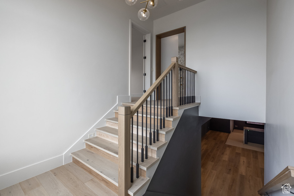 Stairway featuring baseboards, wood finished floors, and a chandelier