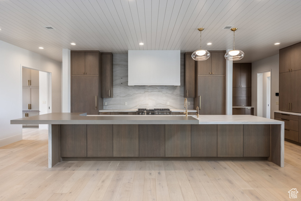 Kitchen featuring tasteful backsplash, a large island, light wood finished floors, and wall chimney exhaust hood