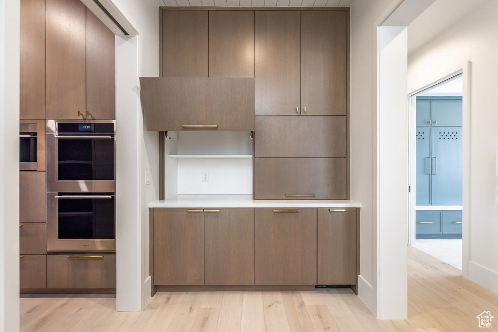 Kitchen with stainless steel double oven, open shelves, light countertops, and light wood finished floors