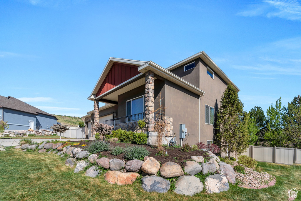 View of property exterior featuring a lawn, fence, stone siding, and stucco siding