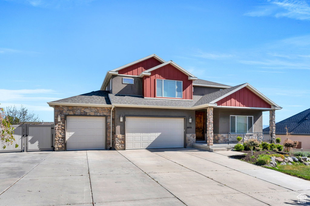 Craftsman-style house featuring covered porch, board and batten siding, concrete driveway, and stone siding