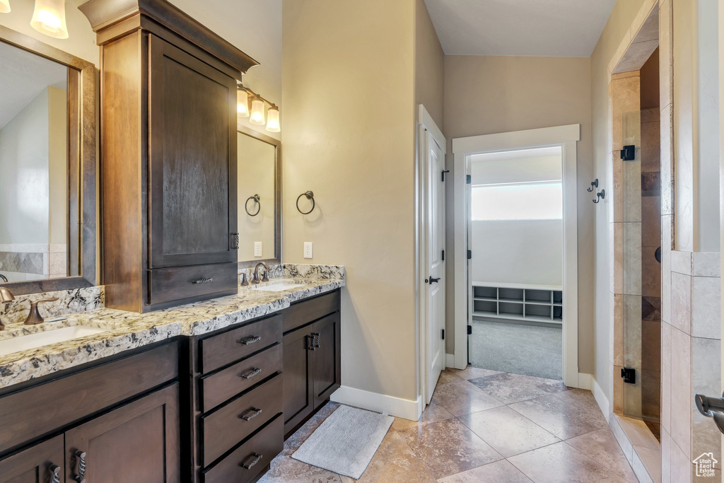 Full bathroom with double vanity, baseboards, and a tile shower