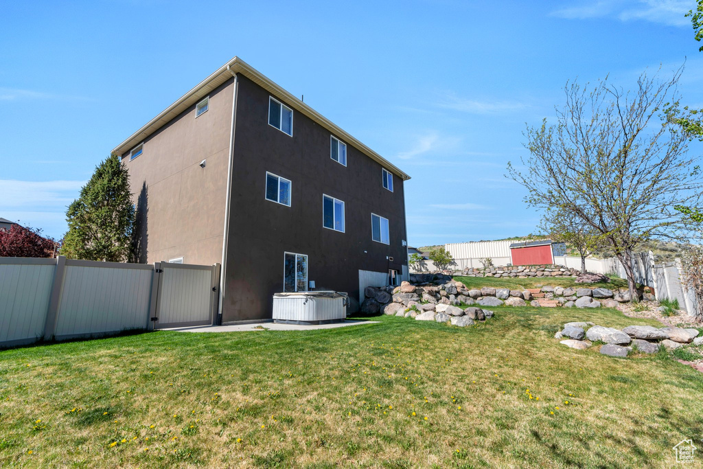 Rear view of property featuring a fenced backyard, a gate, stucco siding, and a hot tub