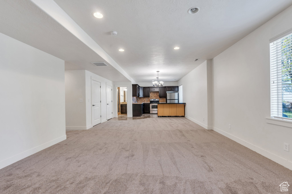Unfurnished living room with a chandelier, baseboards, light colored carpet, recessed lighting, and healthy amount of natural light
