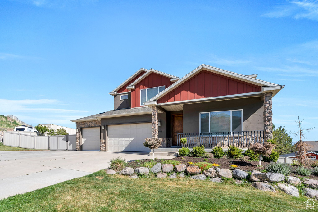 Craftsman inspired home featuring fence, covered porch, stone siding, board and batten siding, and concrete driveway