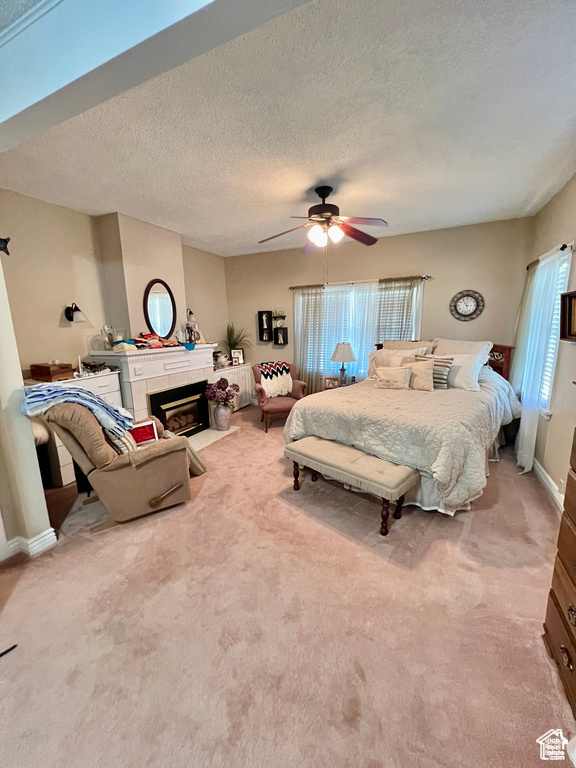 Bedroom featuring a tiled fireplace, carpet floors, a textured ceiling, and ceiling fan