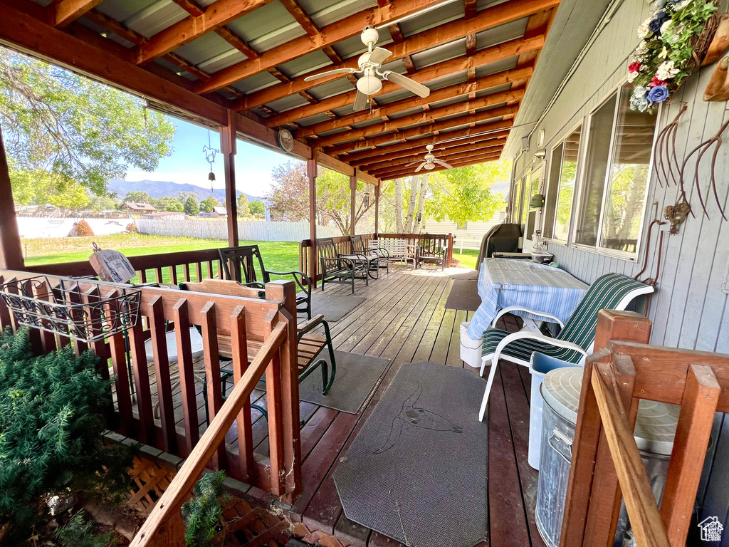 Wooden deck featuring outdoor dining space, a lawn, a mountain view, and ceiling fan