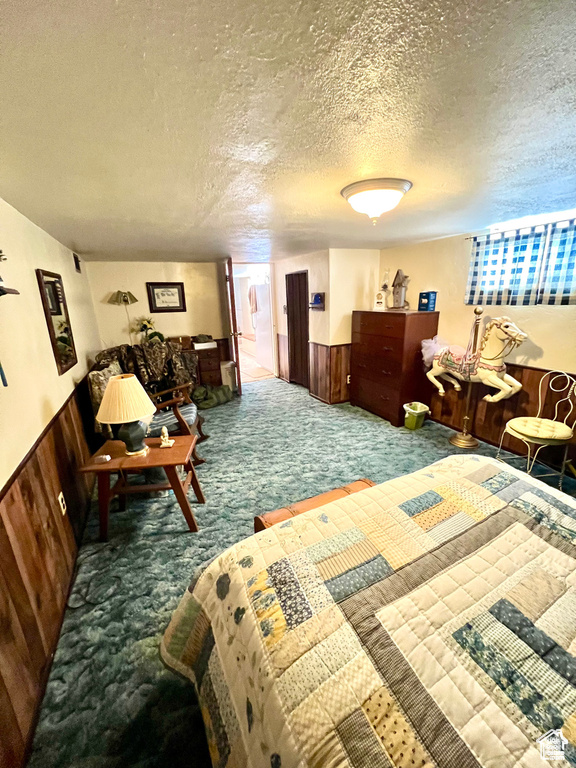 Bedroom featuring a wainscoted wall, wooden walls, carpet flooring, and a textured ceiling