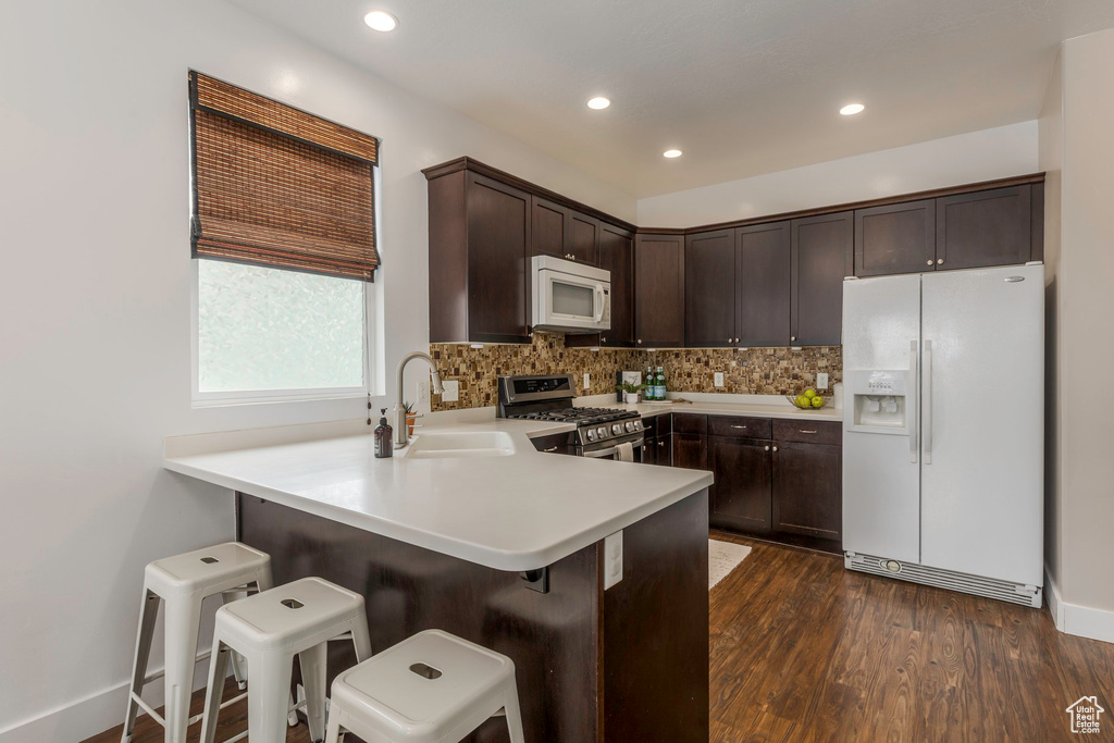 Kitchen with a sink, dark brown cabinets, white appliances, decorative backsplash, and dark wood-style flooring