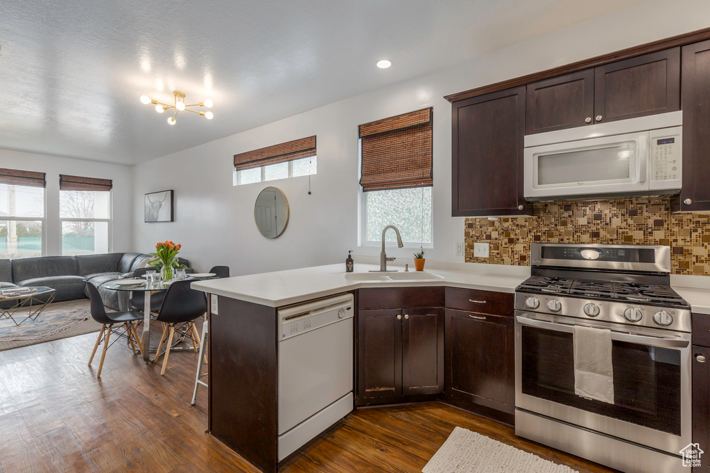 Kitchen with light countertops, dark brown cabinetry, a sink, white appliances, and decorative backsplash