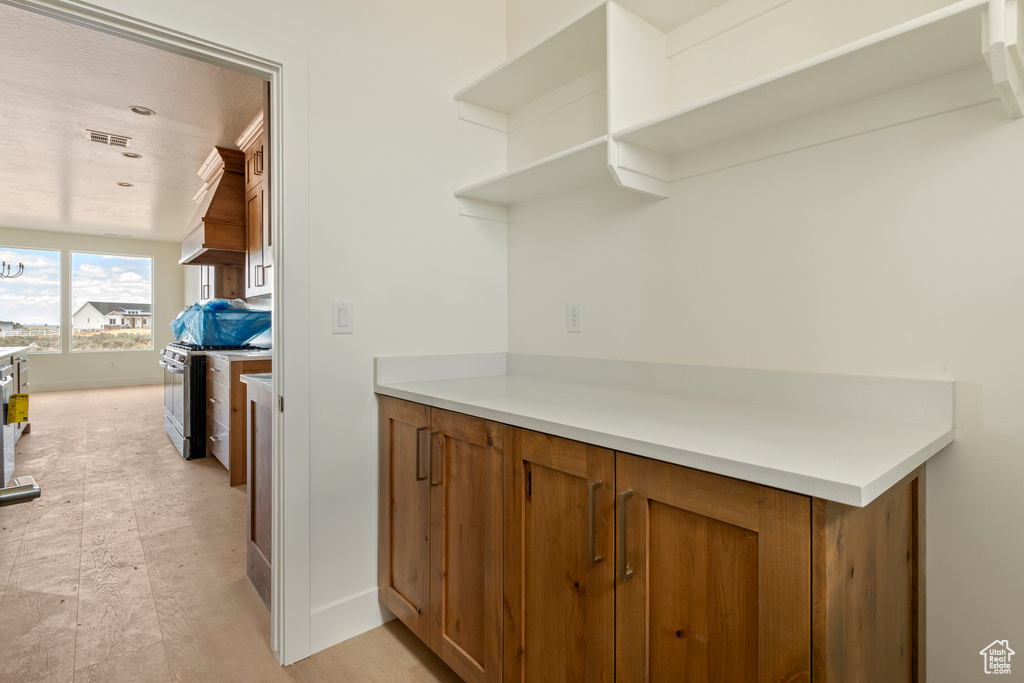 Kitchen featuring open shelves, brown cabinets, stainless steel range with gas stovetop, and light countertops