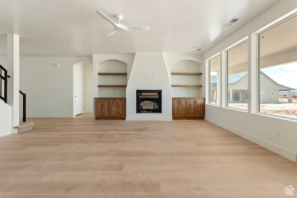 Unfurnished living room featuring stairs, light wood-style floors, a large fireplace, ceiling fan, and baseboards