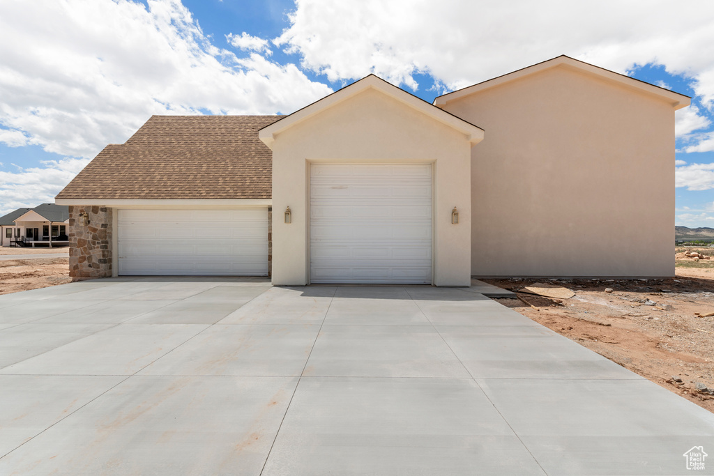 View of front of property with a garage, stucco siding, concrete driveway, roof with shingles, and stone siding