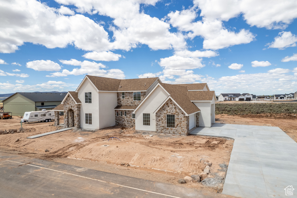 View of front of property featuring stone siding, stucco siding, driveway, and a garage