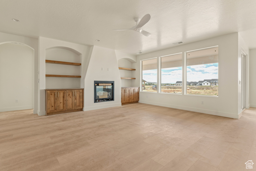 Unfurnished living room featuring a glass covered fireplace, built in shelves, baseboards, and ceiling fan