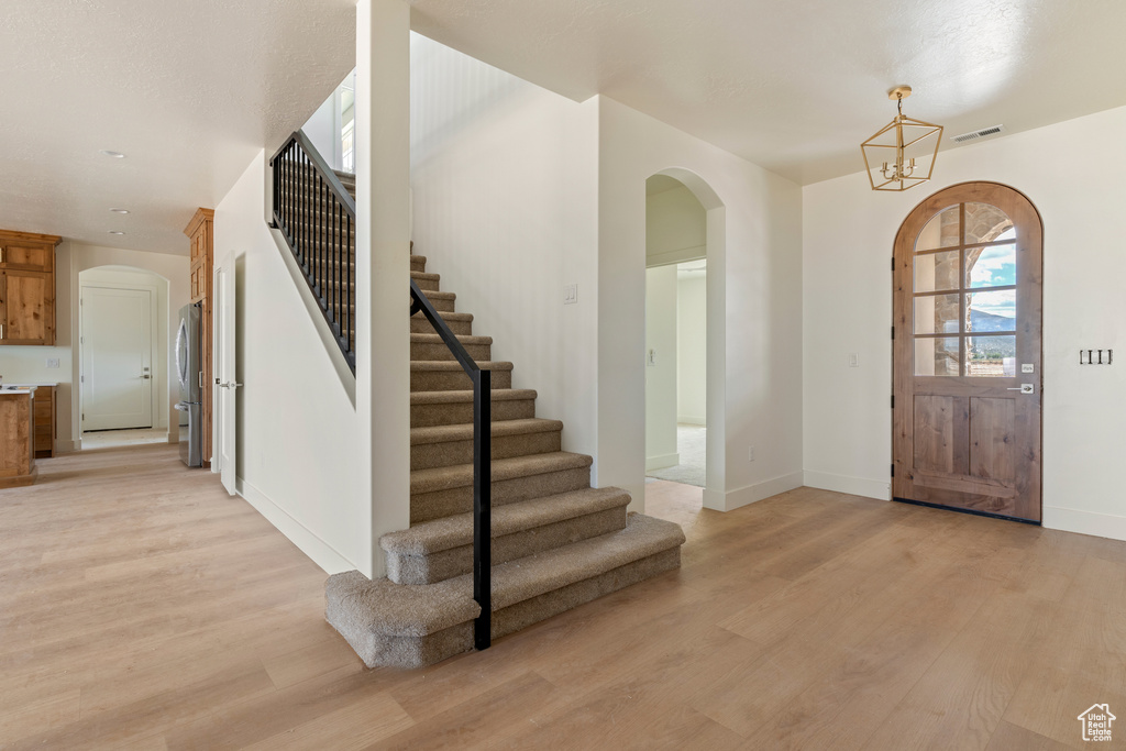 Foyer entrance featuring arched walkways, light wood-style flooring, and stairs