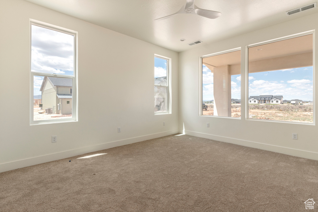 Empty room featuring healthy amount of natural light, carpet flooring, ceiling fan, and baseboards