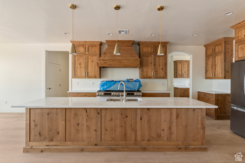 Kitchen featuring custom exhaust hood, freestanding refrigerator, light wood-style floors, light countertops, and brown cabinets