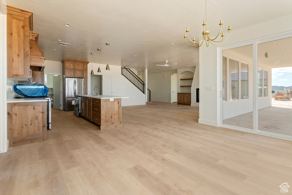 Kitchen featuring open floor plan, freestanding refrigerator, light wood finished floors, an island with sink, and a chandelier