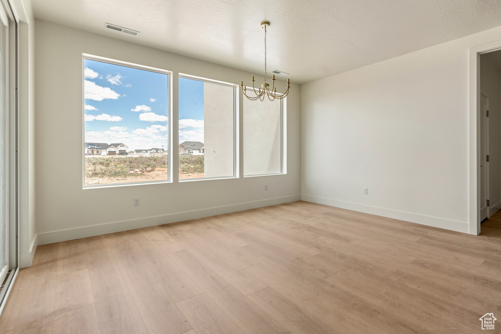 Unfurnished room with a chandelier, light wood-style floors, and baseboards