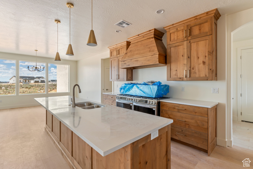 Kitchen featuring custom exhaust hood, a sink, stainless steel gas stove, a large island, and pendant lighting