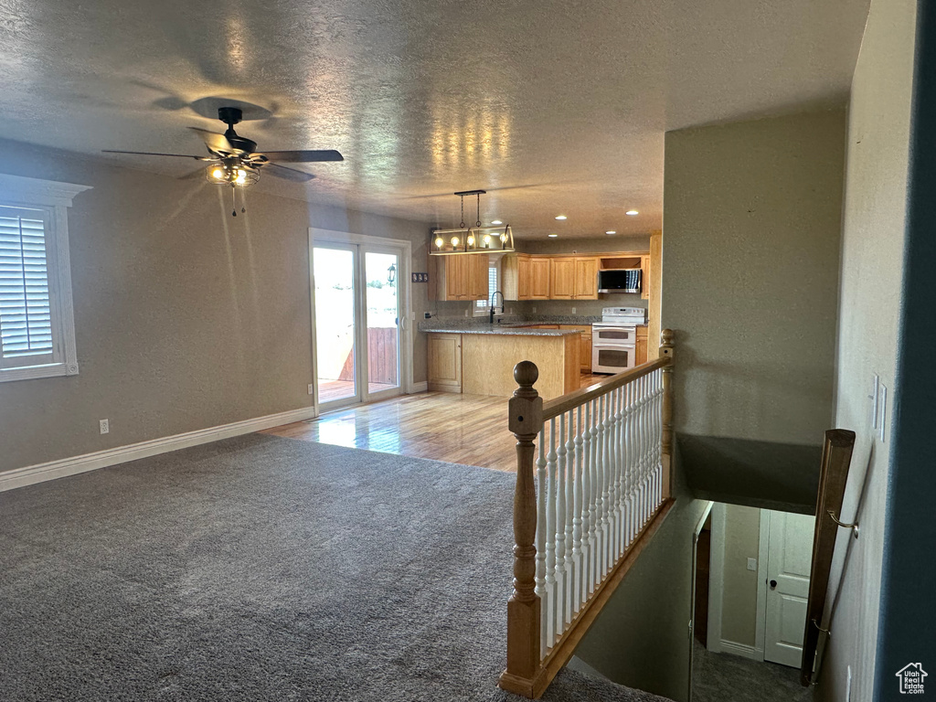 Interior space featuring a ceiling fan, light carpet, a textured ceiling, baseboards, and recessed lighting
