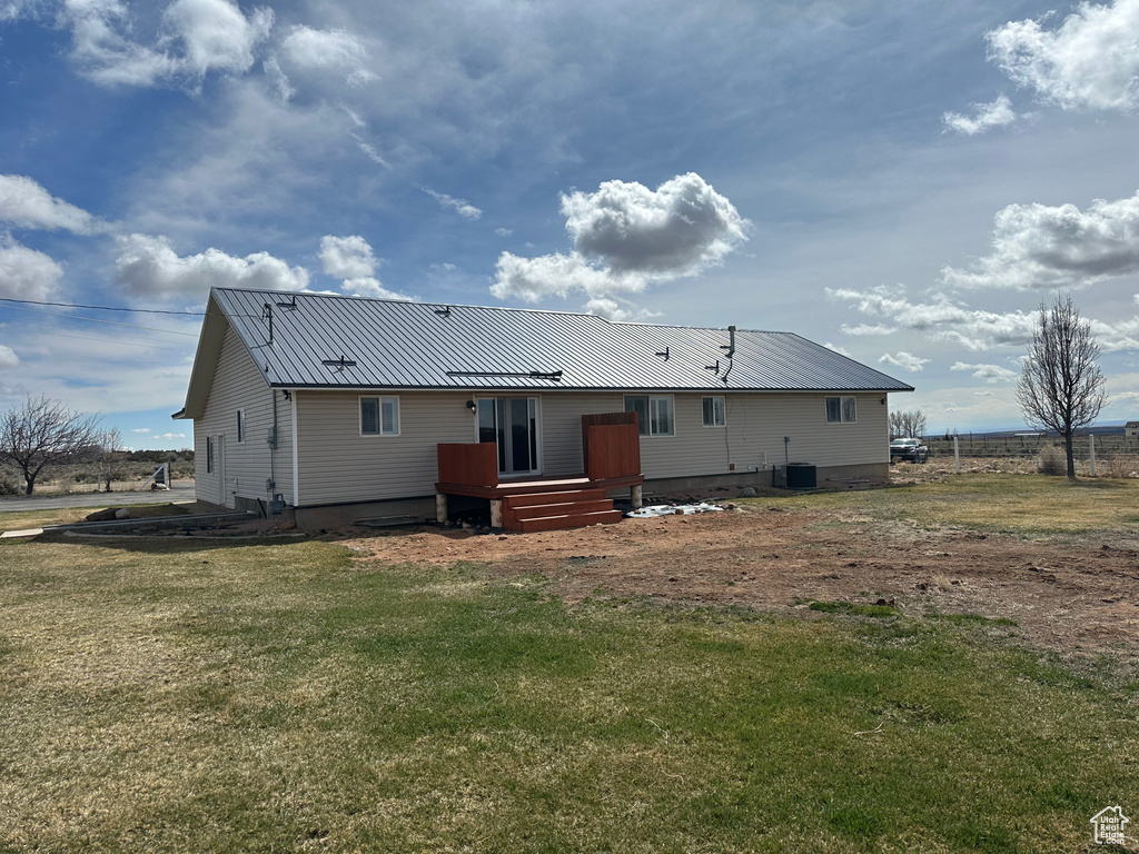 Rear view of house featuring cooling unit, a deck, a yard, and metal roof