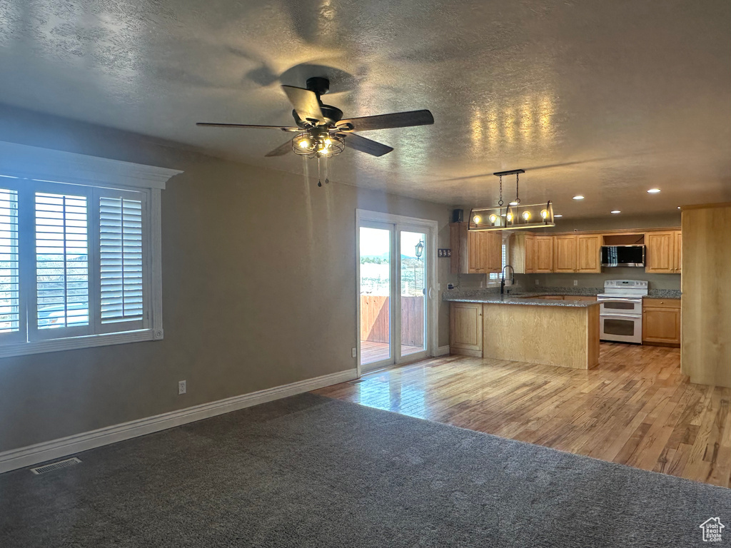 Kitchen featuring double oven range, a peninsula, open floor plan, stainless steel microwave, and ceiling fan with notable chandelier
