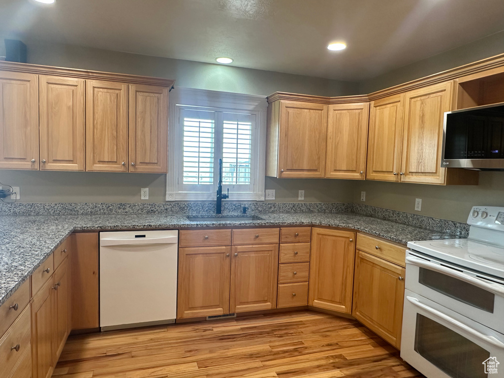Kitchen with light wood-type flooring, recessed lighting, white appliances, a sink, and stone countertops