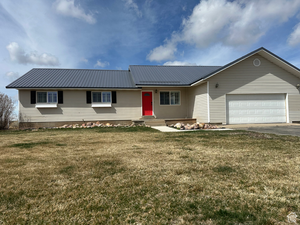 Ranch-style home with a front lawn, aphalt driveway, an attached garage, and metal roof
