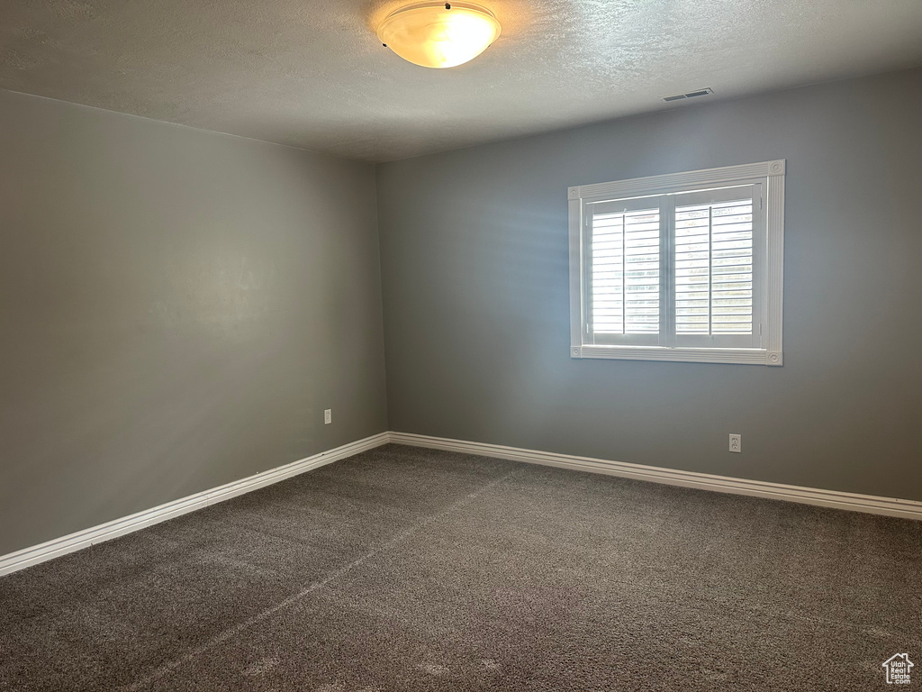 Empty room featuring baseboards, visible vents, dark colored carpet, and a textured ceiling