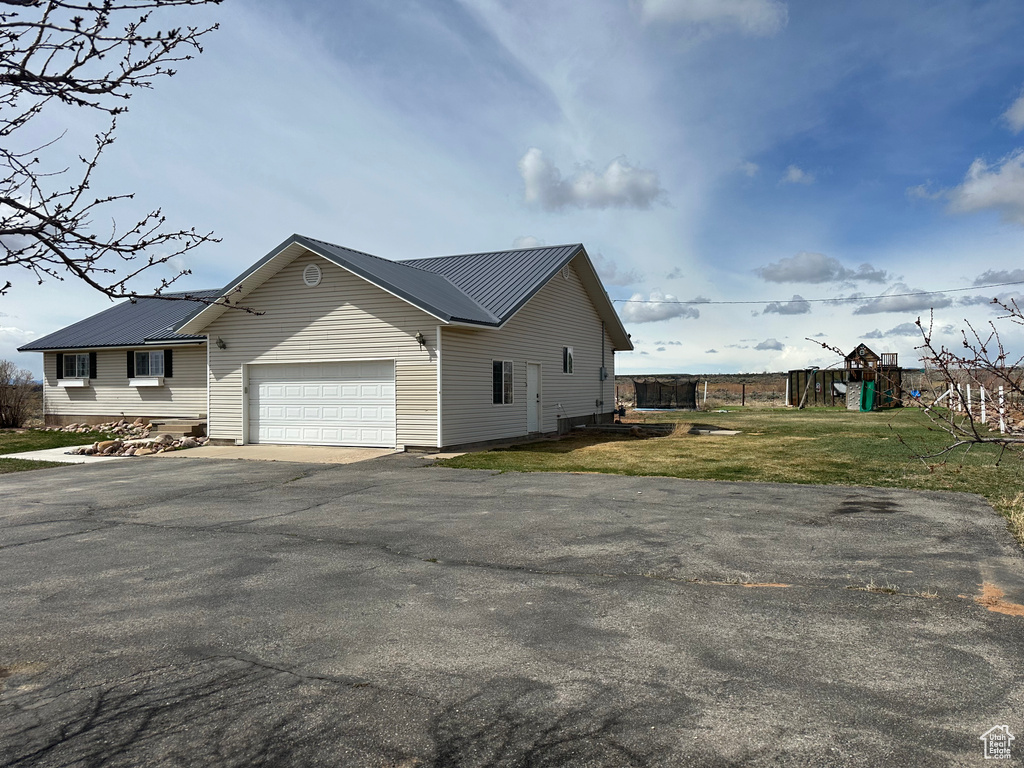 View of side of home featuring metal roof, a playground, a garage, driveway, and a yard