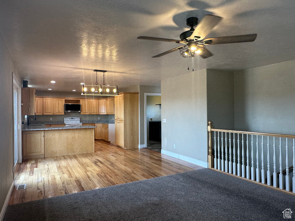Kitchen with a textured ceiling, white electric range, stainless steel microwave, light wood-style floors, and ceiling fan with notable chandelier
