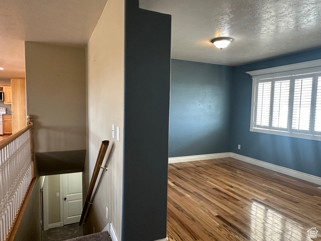 Empty room with a textured ceiling, baseboards, and wood finished floors