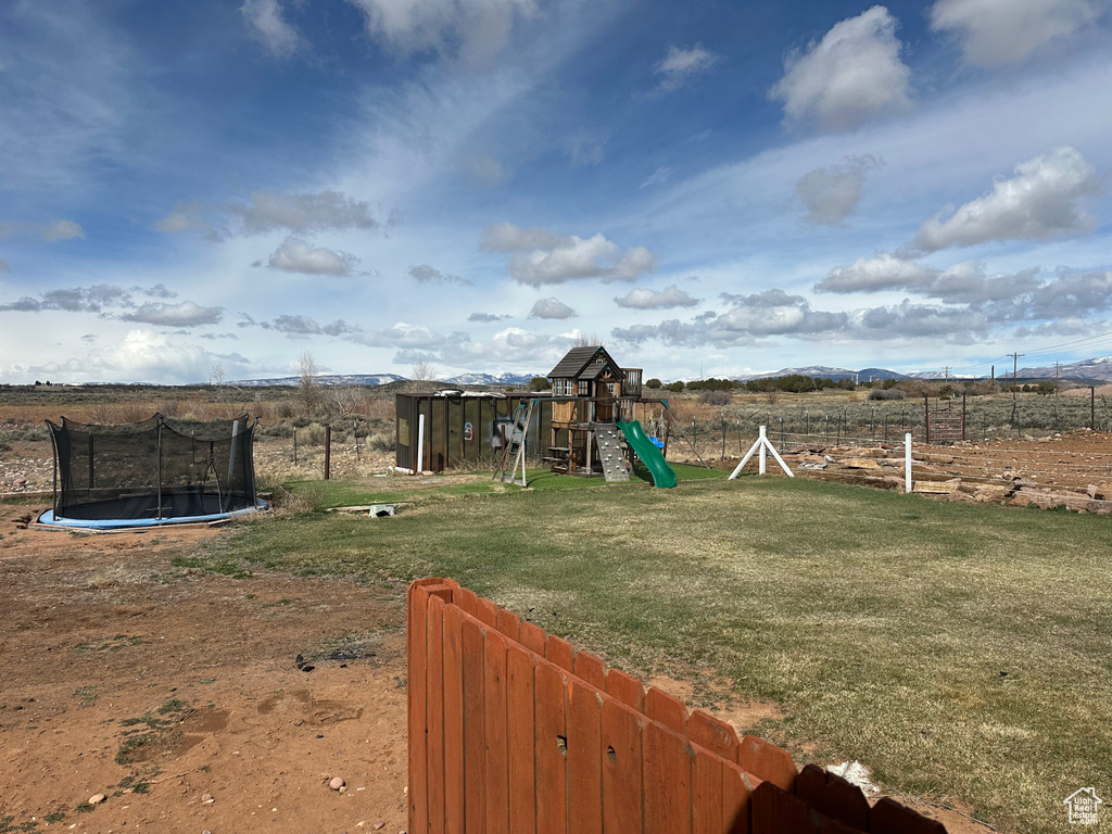 View of yard with an outdoor structure, fence, a rural view, a trampoline, and a playground