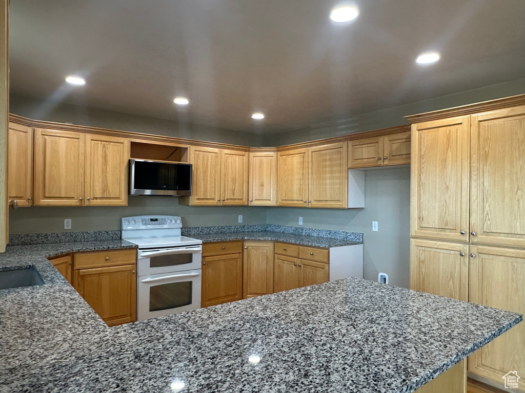 Kitchen with stainless steel microwave, dark stone counters, recessed lighting, and range with two ovens
