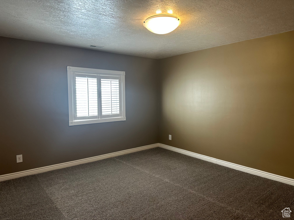 Spare room featuring baseboards, dark colored carpet, and a textured ceiling