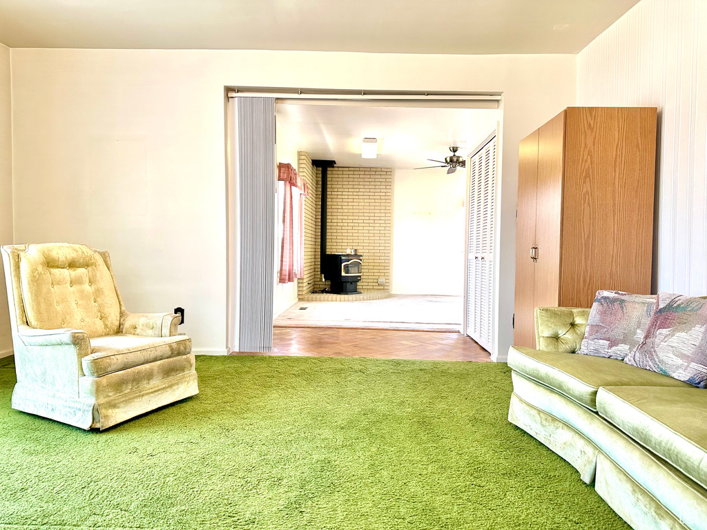 Sitting room featuring a wood stove, carpet floors, and a ceiling fan
