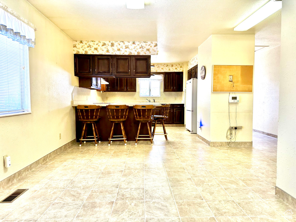 Kitchen with freestanding refrigerator, a breakfast bar area, dark brown cabinets, a peninsula, and light countertops