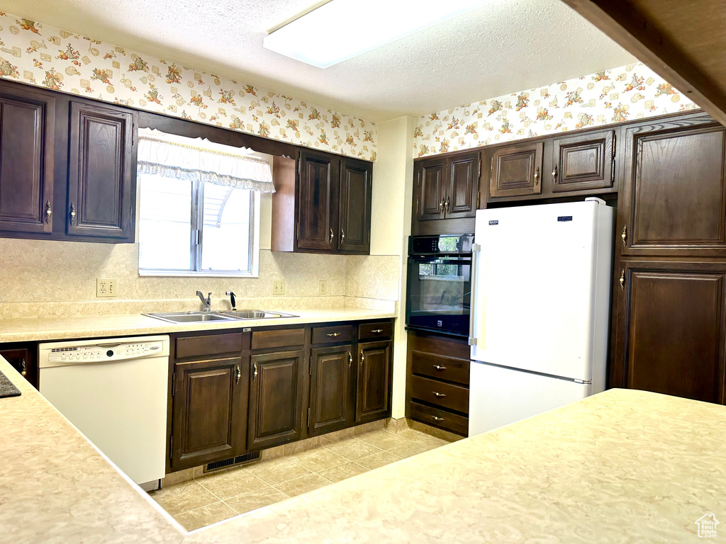 Kitchen featuring white appliances, light countertops, dark brown cabinets, wallpapered walls, and a textured ceiling