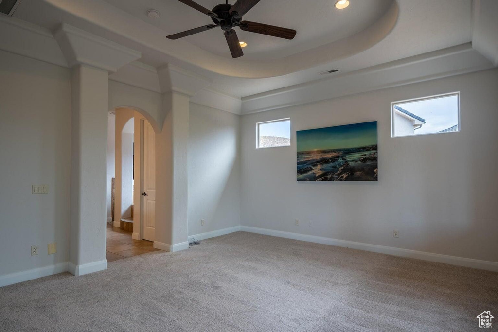 Carpeted spare room featuring arched walkways, a tray ceiling, baseboards, and a healthy amount of sunlight