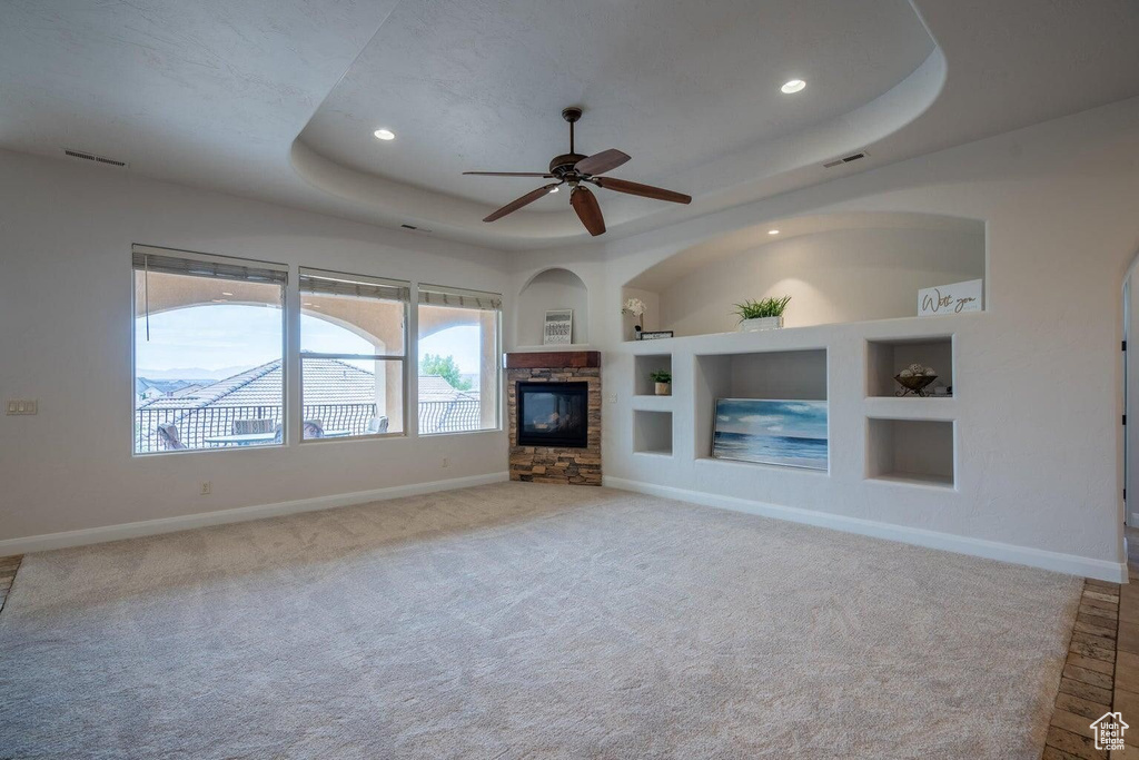 Unfurnished living room with carpet floors, a fireplace, baseboards, built in features, and a raised ceiling