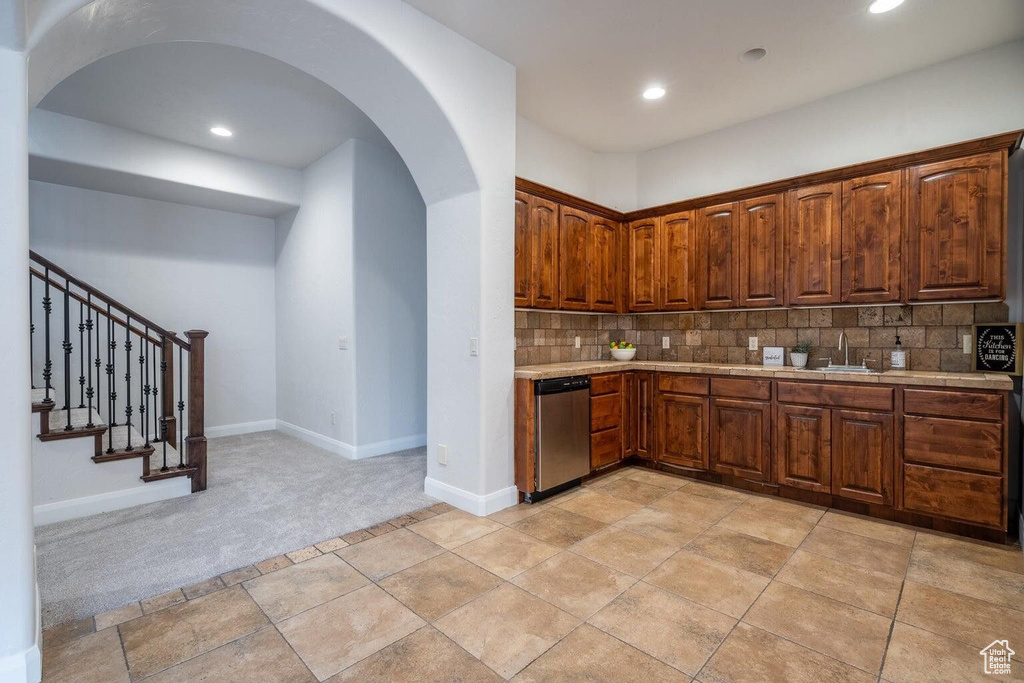 Kitchen featuring tasteful backsplash, arched walkways, dishwasher, light countertops, and a sink