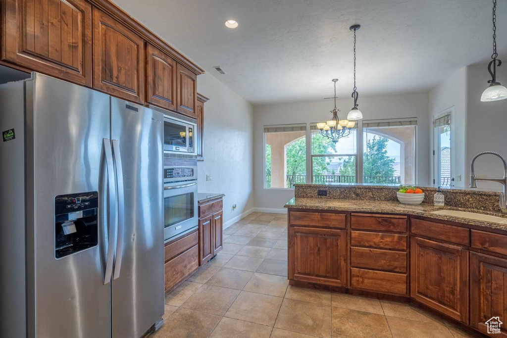 Kitchen with stainless steel appliances, hanging light fixtures, dark stone countertops, and a sink