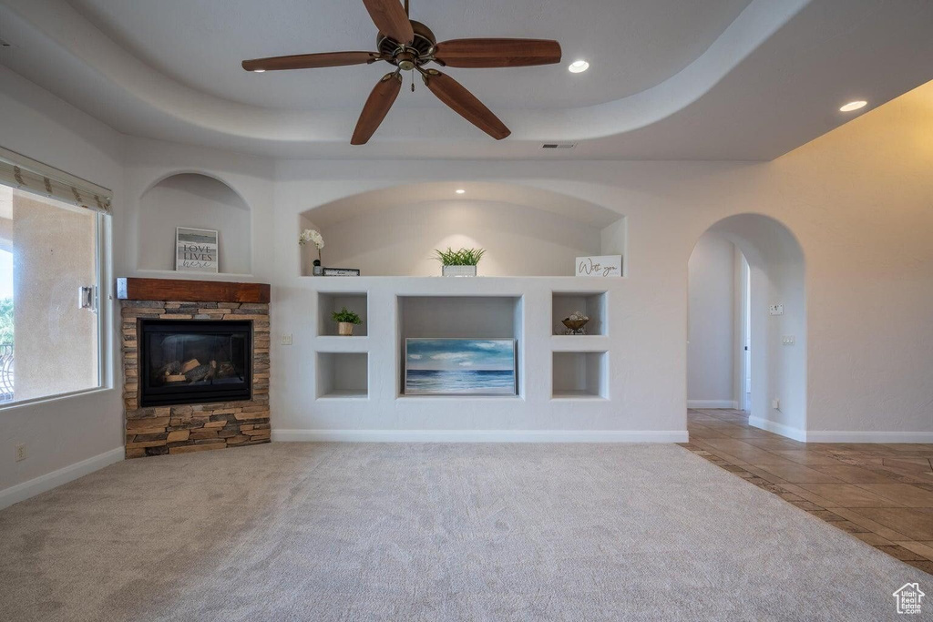 Unfurnished living room featuring built in shelves, a tray ceiling, carpet floors, and baseboards