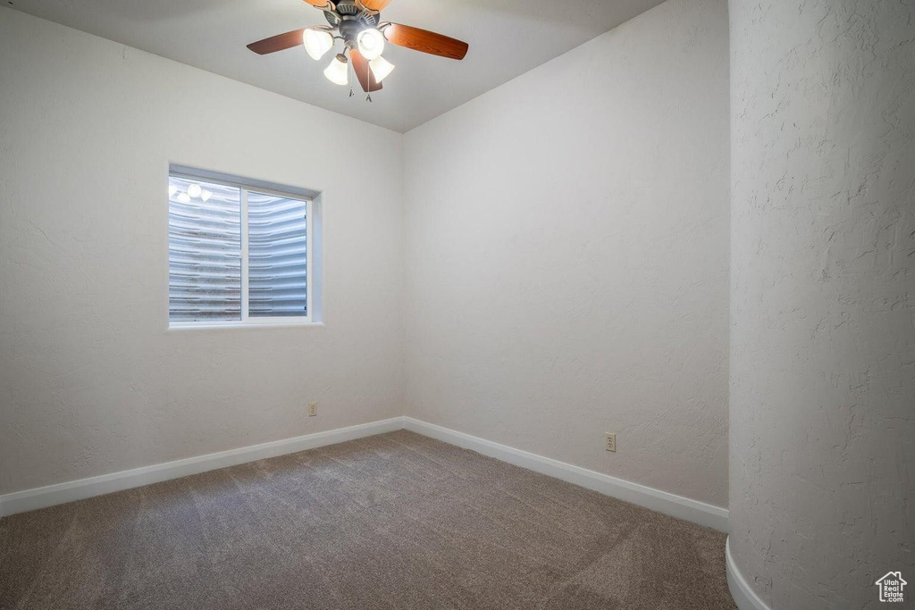 Carpeted empty room with a textured wall, a ceiling fan, and baseboards