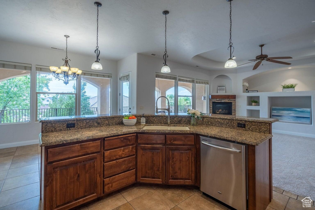 Kitchen with a stone fireplace, a sink, open floor plan, dishwasher, and dark stone countertops