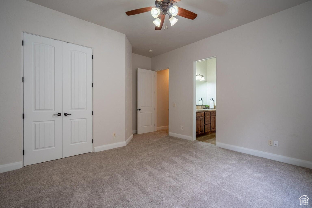 Unfurnished bedroom featuring ceiling fan, light colored carpet, baseboards, a closet, and ensuite bath
