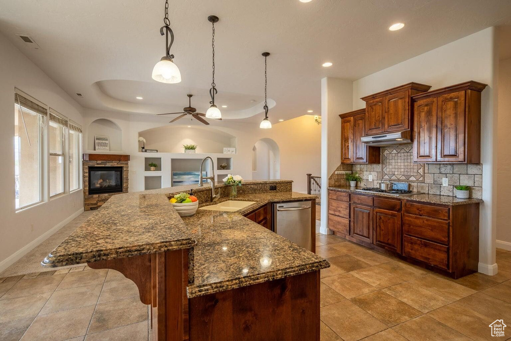 Kitchen featuring arched walkways, under cabinet range hood, a fireplace, a sink, and appliances with stainless steel finishes